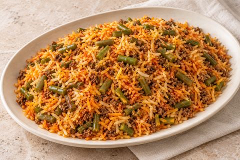 Separate tomato-colored rice grains with green beans and cooked beef crumbles; AI illustration.